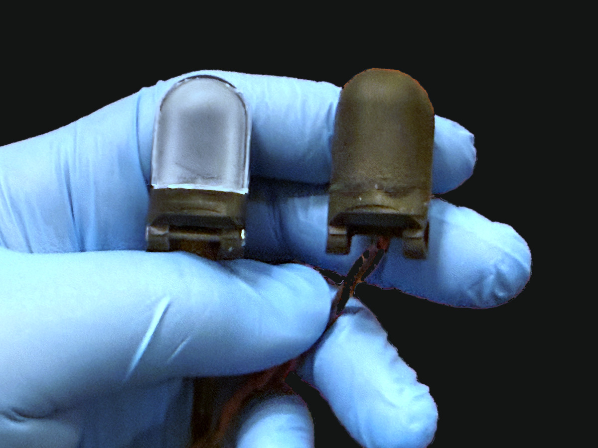 Two humanoid fingertip sensors held in a gloved hand, one with its gel exposed and one covered by the membrane